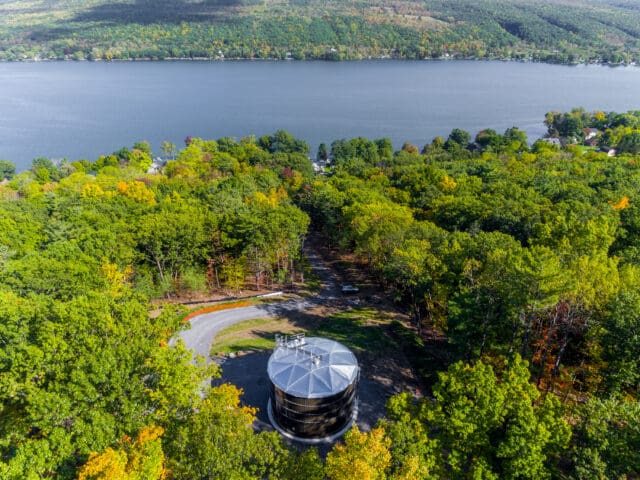 An aerial photograph of a water tank surrounded by trees with a lake in the background.