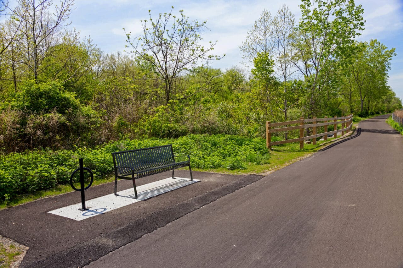 A photograph of a bench along a paved trail