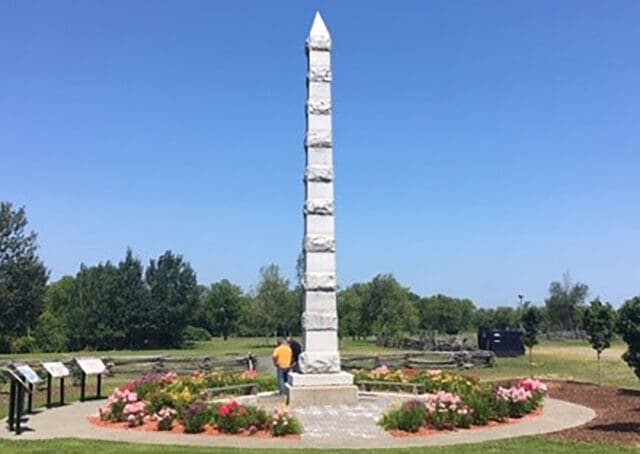 A photograph of a tall, thin monument among flowers