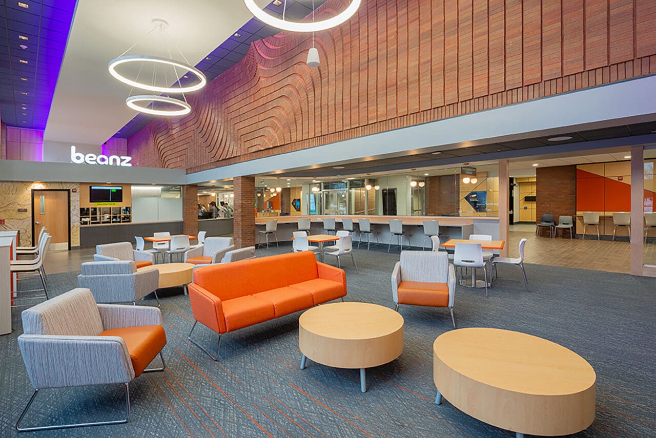 A photograph of a school building lobby with a cafe called Beanz in the background. The furniture and fixtures have an orange theme and are modern.