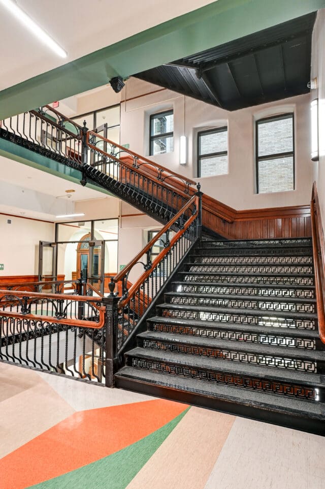 A photograph of a staircase made of black iron in very intricate designs. The railings are wooden.
