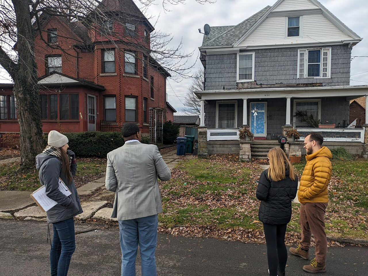 A team of people with clipboards standing in front of a house collecting data for a housing survey.