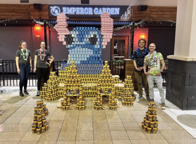 Four people stand aside a structure built of canned goods, a replica of Stitch, from the movie, Lilo and Stitch.
