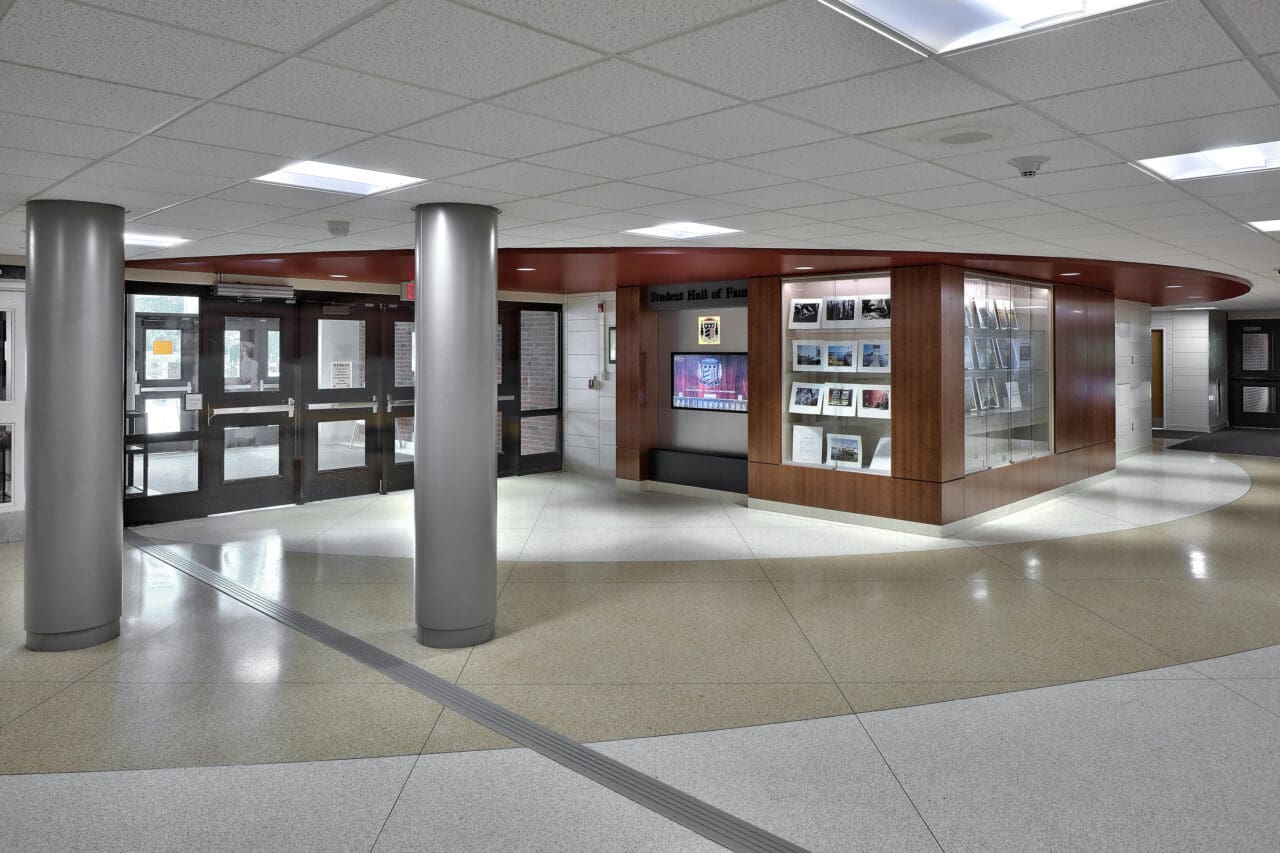 A photograph of the entry to a school from the interior where a digital display cases and two traditional display cases show student artwork.