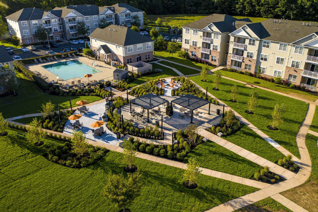 A photo of a central gathering area at an apartment complex including walking paths, seating, pergolas, and greenery