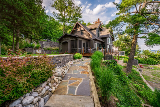 A photo of a stone walkway surrounded by curated plantings leading up to a coastal home with a cabin-feel