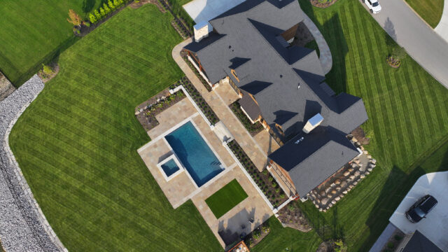 Aerial photography of a single-family home with an emphasis on the outdoor living space, including a pool, hot tub, and stone patio
