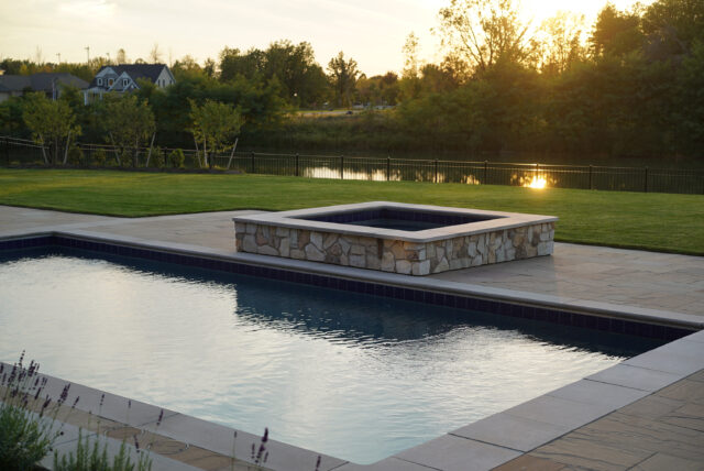 A photo of a hot tub overlooking a pond as part of an outdoor living space behind a single-family home.