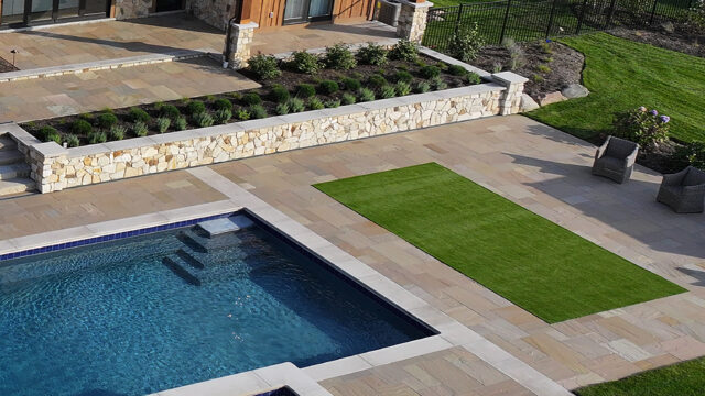 A photo of a small turf field adjacent to an in-ground pool in the outdoor living space of a single-family home.