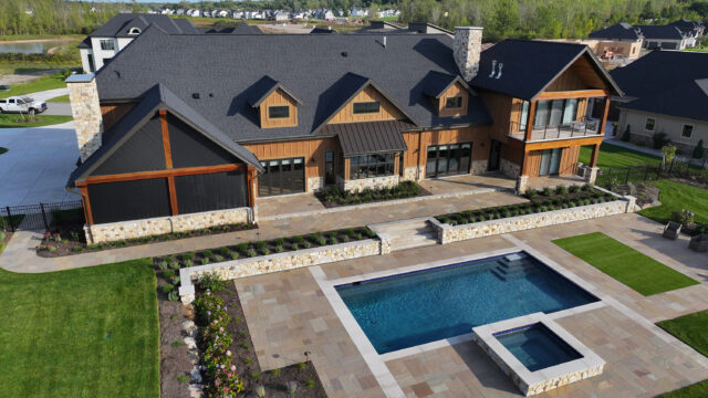 A photo of an outdoor living space behind a single-family home, including an in-ground pool, hot tub, and stone patio