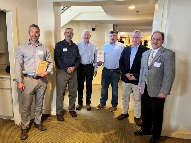 A photograph of six people standing together, two are holding wooden placards.