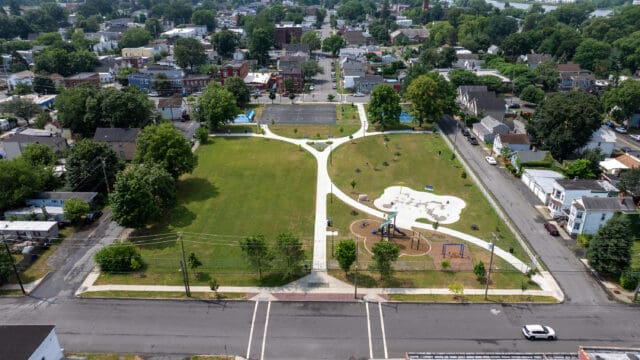 An aerial photograph of a park with a walking path, a playground, a splash pad, and two basketball courts visible.
