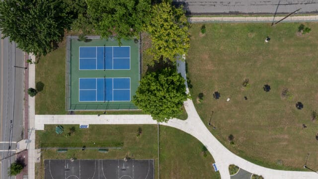 An aerial photograph of a park with a walking path, two tennis courts, and two basketball courts.