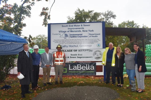 A photograph of eight people in front of a sign for a groundbreaking