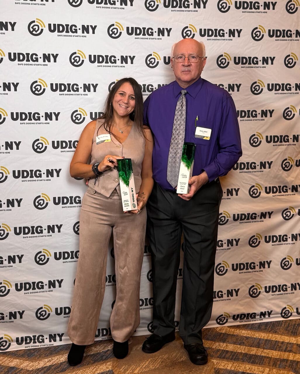 A photograph of two people holding awards in front of a banner