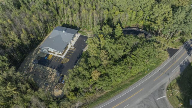 An aerial photograph of a building, parking lot, and driveway among trees