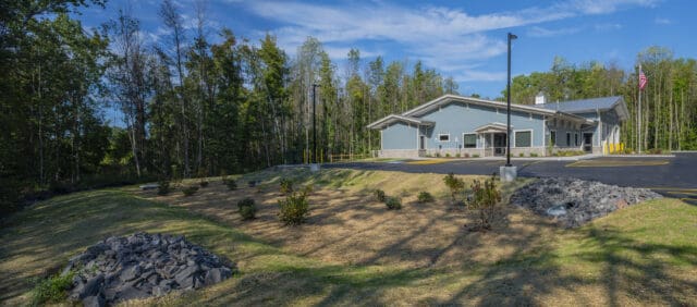A photograph of a bioretention pond at an elevation just below the Wayne County EMS Sodus Substation, which is pictured in the background.