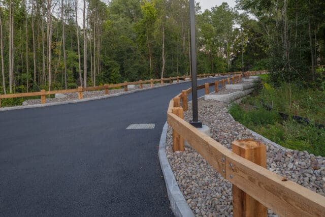 A photograph of a driveway lined by wooden guard rails, stone, and retaining walls.
