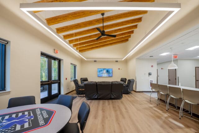 A photograph of a lounge area with high ceilings, leather furniture, a table with chairs, and doors leading outside.