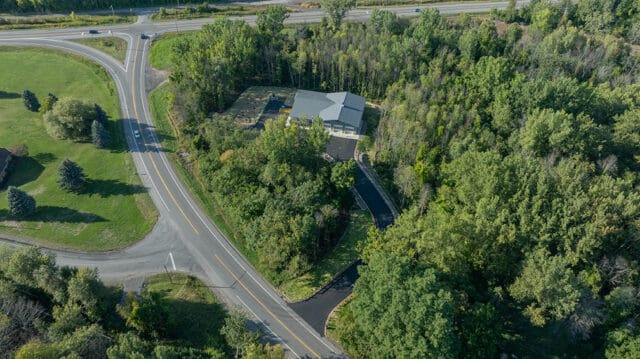 An aerial photograph of a building and driveway among trees between two roads.