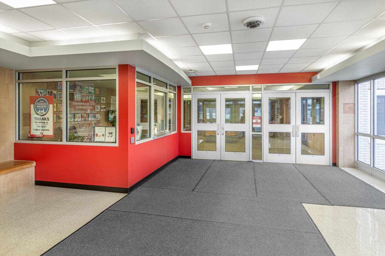 A photograph of a secure vestibule at the entry doors to a school. A security camera is on the ceiling.