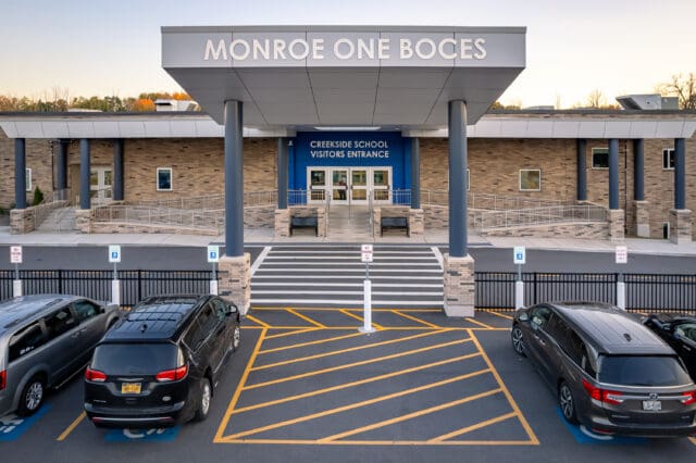 A photograph of the visitor's entrance to Creekside School at Monroe One BOCES. A crosswalk, stairs, and ramps lead to the entry.