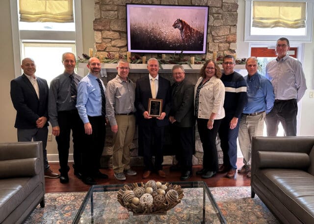 A photograph of ten people, the person in the middle is holding an award