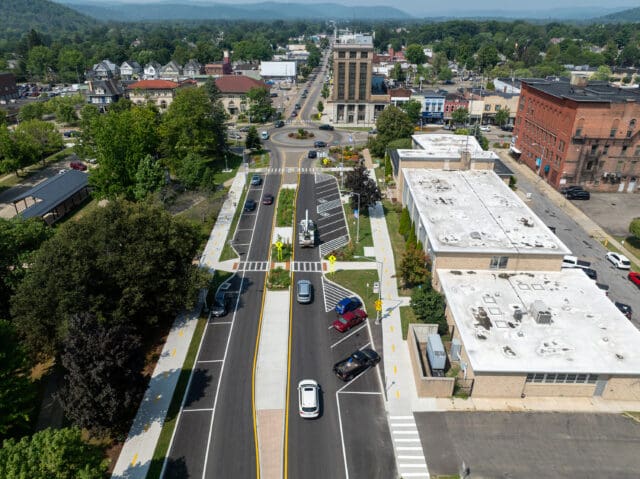 An aerial photograph of a two-way road and streetscapes with parking, sidewalks, crosswalks, and a traffic circle