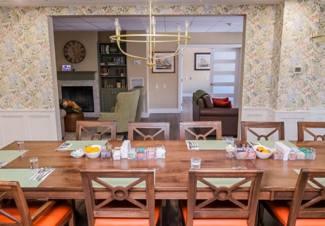 A photograph of a dining room table with a large chandelier above and looking to a living room
