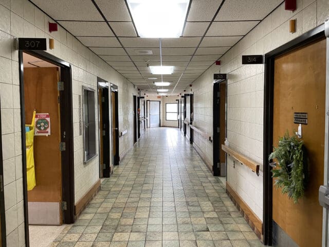 A photograph of a dated hallway in an assisted living facility with multiple doors.