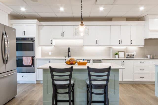 A photograph of a modern kitchen with white cabinets, stainless steel appliances, and blue island.