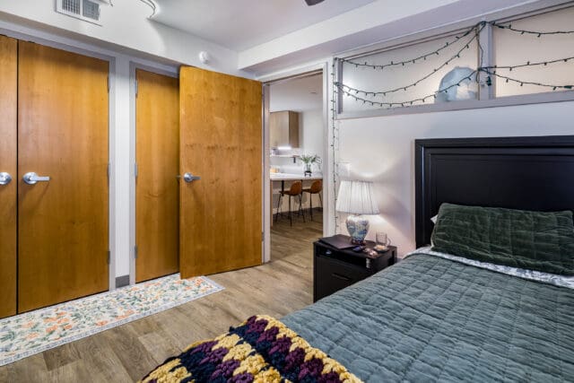 A photograph of a bedroom looking into a kitchen