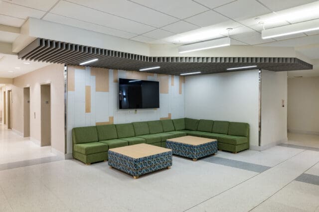A photograph of a building lobby with a large, green modular couch and two large coffee tables.