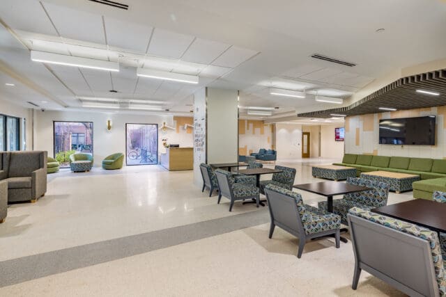 A photograph of a building lobby with a variety of seating styles in multiple seating clusters. A circulation desk and two televisions are visible.