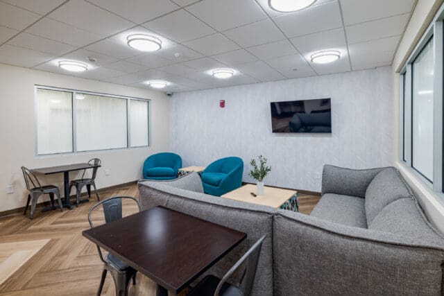 A photograph of a common area with tables, chairs, a couch, and television.