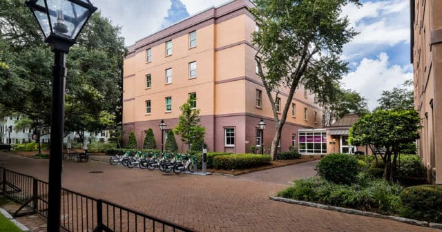 A photograph of the exterior of a four-story building with a courtyard and bicycle rack surrounding it.