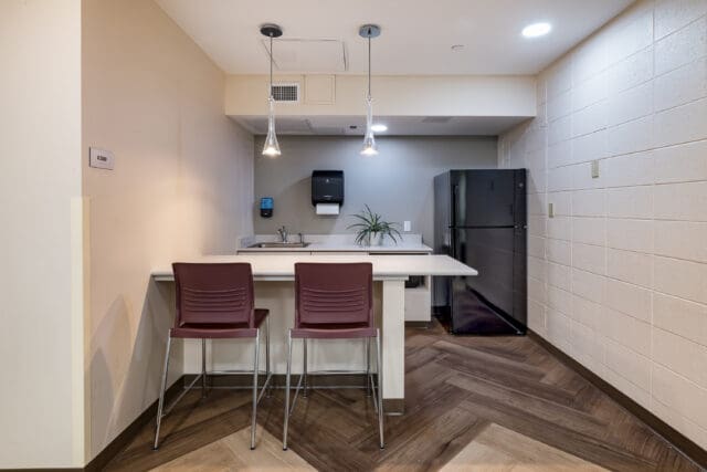 A photograph of a small kitchenette with modern finishes, a kitchen island, and two chairs.