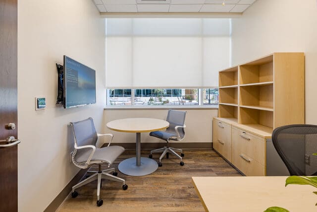A photograph of an empty office. A table with two chairs, a television, and an empty cabinet are visible.