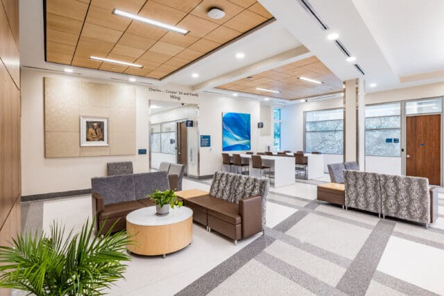 A photograph of a bright, modern lobby. Multiple seating clusters include couches and small tables.