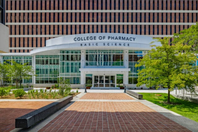 A photograph of the exterior of a modern building with brick pathways and landscaping leading to the entry. Signage says, 