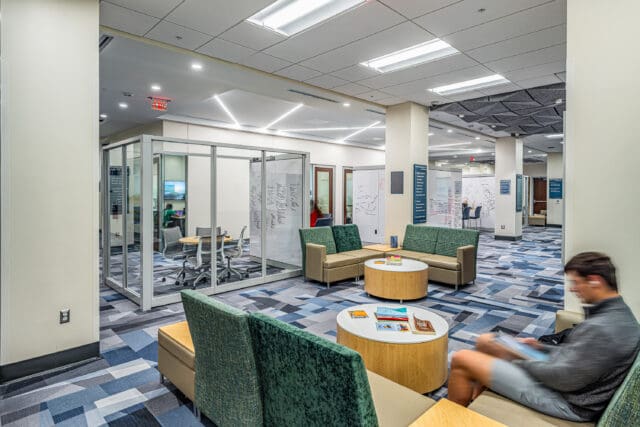 A photograph of a seating area amongst breakout rooms that have glass walls and one wall made of dry-erase board.