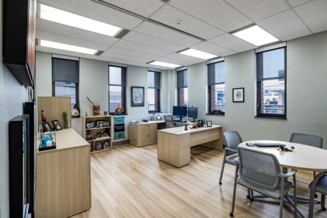 A photograph of an office with multiple windows, desks, and personal items.