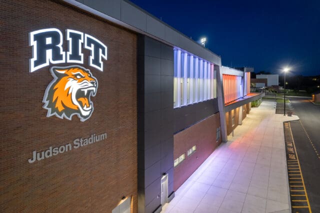 An aerial photograph from an angle looking down the front of an athletic stadium with the RIT logo and