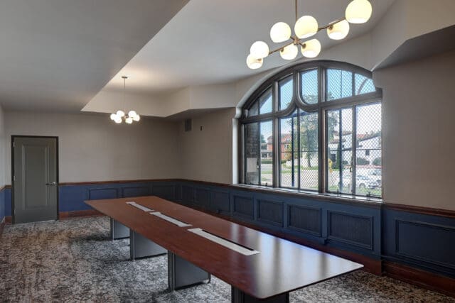 A room with unique windows, modern lighting, and a large conference table at the center.