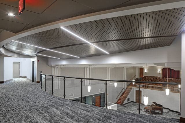 A photograph from a second floor mezzanine of an open room. Another mezzanine is visible in the background beyond a glass railing.