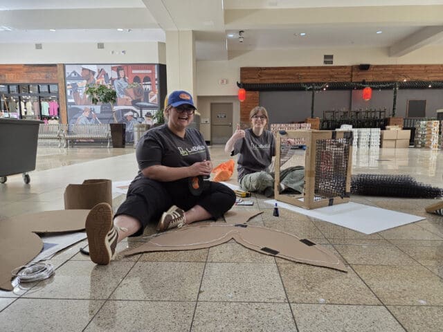 A photograph of two people sitting on the floor making things out of cardboard.