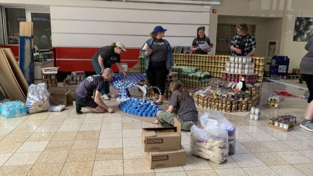 A photograph of multiple people building a structure out of non-perishable items.