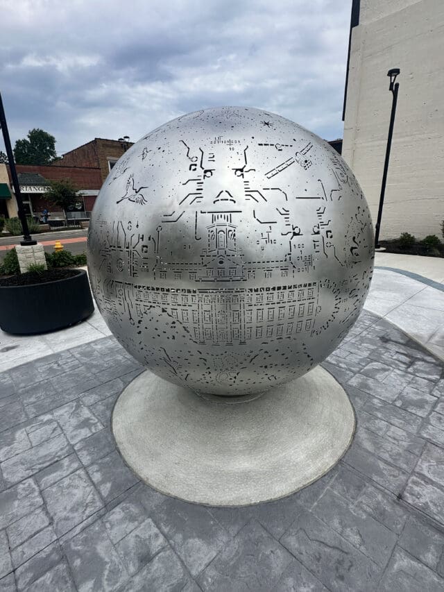 A photograph of a steel sphere with artwork laser-cut in