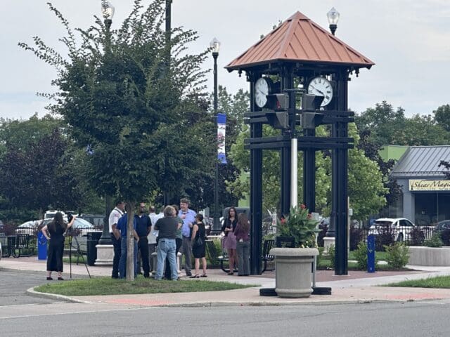 A photograph of people gathered near a clock tower in a small park setting.