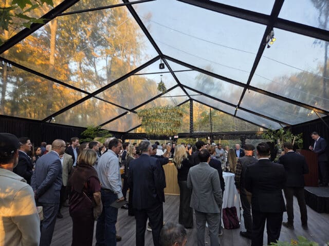 A photograph of people standing about in a pavilion with a clear roof.